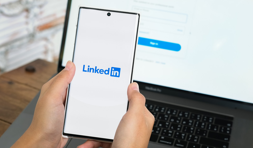 Smartphone displaying LinkedIn login screen in front of a laptop